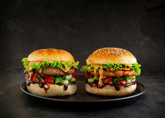 Fresh tasty burgers with chicken and pork on dark background. Fat unhealthy street food.