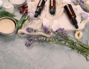 Bottle of essential oils with herbs and flowers on light gray background.