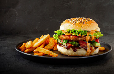 Fresh tasty burger with chicken, salad, cheesee, sauces and with french fries on dark background....