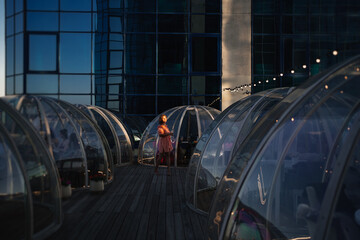 at sunset. woman in a pink dress strolls along the roof between the igloo tables