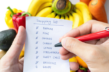 Hands hold shopping list checking with variety of colorful fresh fruits and vegetables. Raw organic...