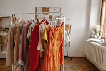 Photo of colorful summer stylish clothes on hanger. Snapshot of cozy white room. Interior of fashion designer office.