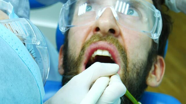 Close-up of a woman dentist in special uniform giving a fluoridation procedure to a man
