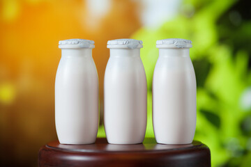 Natural liquid yogurt with probiotics in small plastic bottles on wooden table on background of green trees.