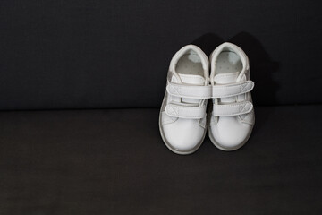 High angle view of a pair of white sneaker of baby. Children shoes isolated on black background with copy space. 