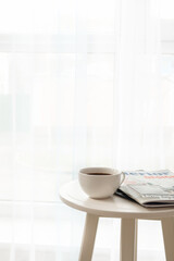 Table with coffee cup and magazines near light curtains