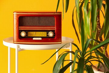 Retro radio receiver on table and houseplant near color wall