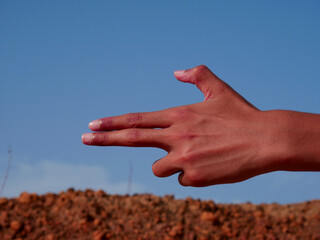 Boy hand on gun shape presented on blue sky background.