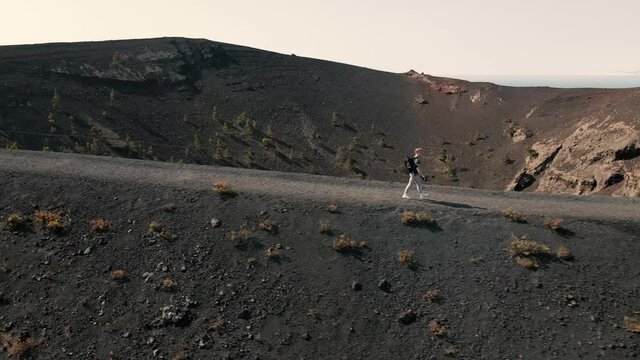 Panoramic aerial shot tracking a person hiking over a volcanic mountain path