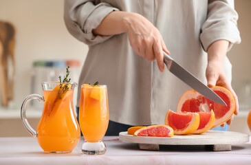 Woman cutting grapefruit on table in kitchen