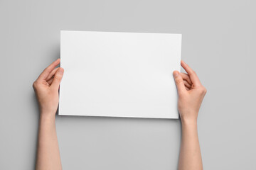 Woman holding blank sheet of paper on grey background