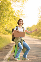 Young woman with cardboard hitchhiking on road