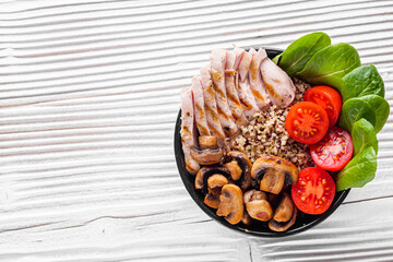 bowl of healthy quinoa with grilled chicken and vegetables on a white rustic wooden background