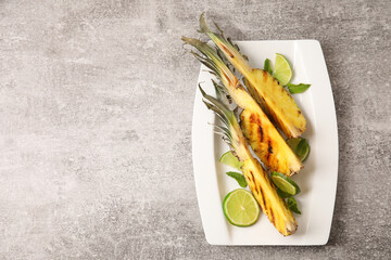 Plate with grilled pineapple slices and lime on grunge background