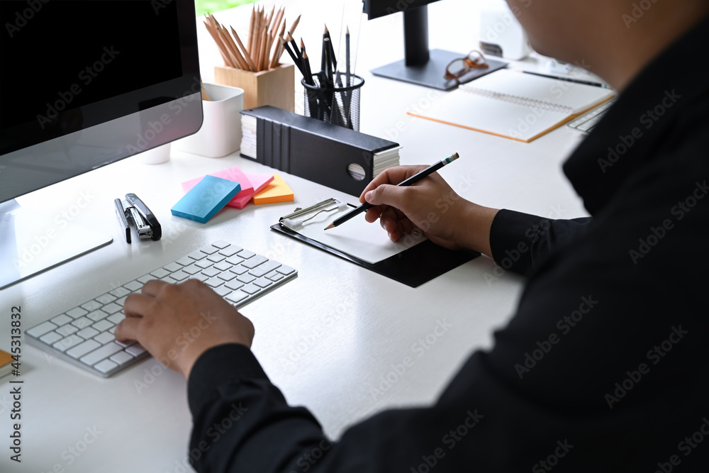 Poster cropped shot businessman working with computer and making note on notebook.