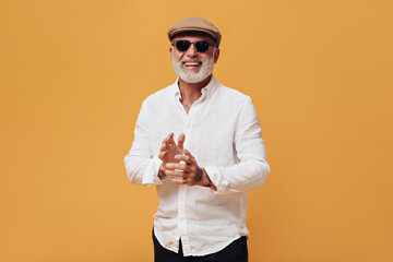 Portrait of man in eyeglasses, cap and white shirt. Smiling adult guy with gray beard posing and...