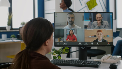 Handicapped invalid disabled business woman discussing during video conference with partners using computer and headphone, working in financial startup office sitting immobilized in wheelchair