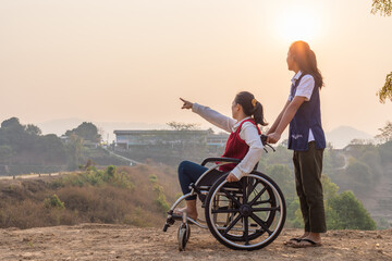 Disabled handicapped woman in wheelchair walking with his care helper in sunset.