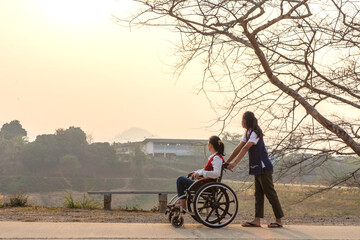 Disabled handicapped woman in wheelchair walking with his care helper in sunset.