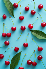 Cherry pattern. Flat lay of cherries and green leaves on blue background. Top view