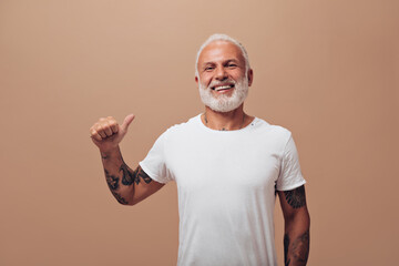 Smiling adult man looks into camera on beige background. Handsome guy with gray beard in white...