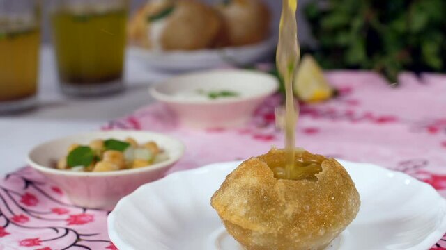 Spicy / sweet Pudina / tamarind water falling inside a crispy Phuchka on a plate - Street Food from India. A bunch of fresh mint leaves  green chilies  sliced lemon - Gol Gappa / Phuchhka