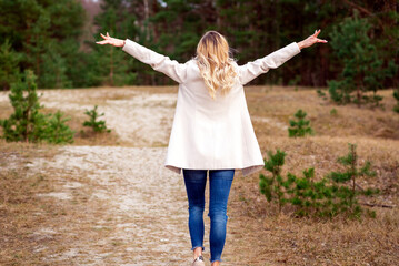 One young beautiful blonde long haired woman with raised hands over green natural forest background outdoor.