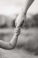 The child holds his mother's hand tightly. Black and white photo of the child with his mother. Close-up of the child's and parent's hands. A place for a text about childhood