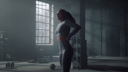 Fototapeta na wymiar Sportswoman standing in modern gym. Exhausted girl taking break after training