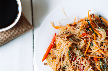 Top view of plate with salad and cup with soy sauce on white wooden background