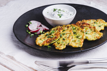 Zucchini pancakes with yoghurt and radish on black plate