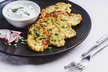 Zucchini pancakes with yoghurt and radish on black plate