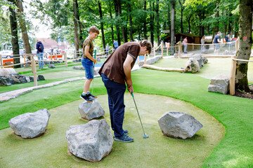 School kid boy playing mini golf with father. Happy child and dad, young man having fun with...