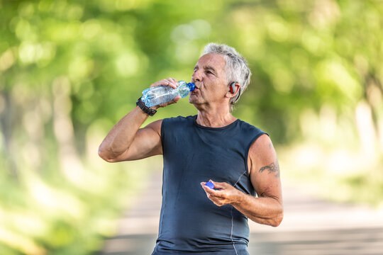 Handsome elderly man rehydrates after a run outdoors in the nature by drinking water from a bottle