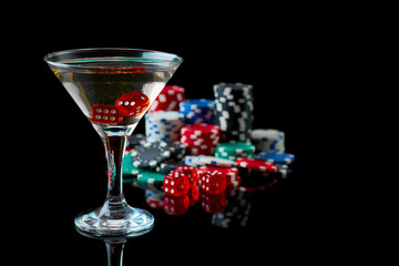 Stack of Casino gambling chips, glass of martini vermouth and red dices isolated on reflective black background