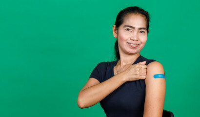 Fototapeta na wymiar Middle aged Asian woman smiling showing her arm with bandage patch showing she got vaccinated for Covid 19 virus on green background. Concept for Covid 19 vaccination