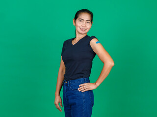 Middle aged Asian woman smiling showing her arm with bandage patch showing she got vaccinated for Covid 19 virus on green background. Concept for Covid 19 vaccination