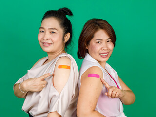 Two middle aged Asian women showing their arms with bandage patch showing they got vaccinated for...