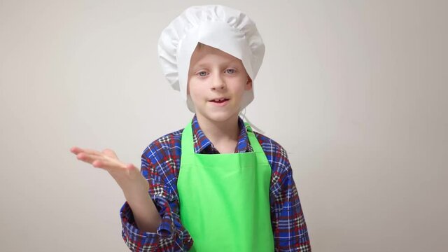 little cook boy in green apron and chef's hat stands and shows sign of belissimo idea of cooking new dish hobby schoolboy in cook's costume kitchen food restaurants public catering cooking food