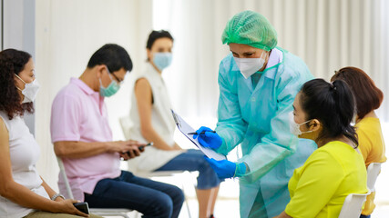 Group of diverse citizens wear face mask in Coronavirus vaccinating queue line sitting checking his...