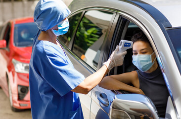 Female doctor in blue hospital uniform and face mask stand near drive thru car queue hold infrared...