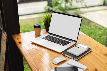 Computer laptop mock up image blank screen with calculator, coffee cup on wooden table at cafe co-working space