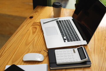 Laptop with black empty screen mockup, calculator, and stuff on wooden table