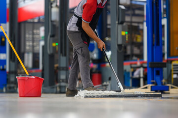 Car mechanic cleaning the garage floor at the auto industry shop workshop Use a mop to clean water...