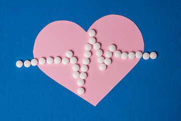 Heart pulse is lined with small white pills on a paper pink heart background.