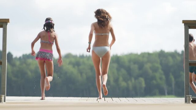 Happy family have vacations at the lake. Mother with daughter and son jump from the pier together. Boy and girl diving from the dock into the water. Children having fun.