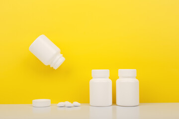 Creative composition with vitamins bottles on white table against yellow background. Flying opened...