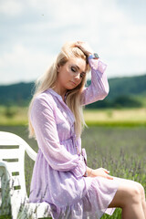 Fototapeta na wymiar Beautiful blonde woman in a field on a white chair, summer dress