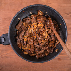 Fried beef with mushrooms in a pan, top view