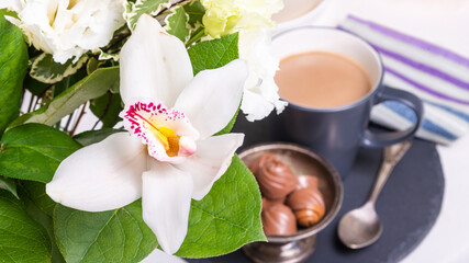 Romantic breakfast - White orchid in a bouquet close-up against the background of a cup with cocoa and sweets in a vase